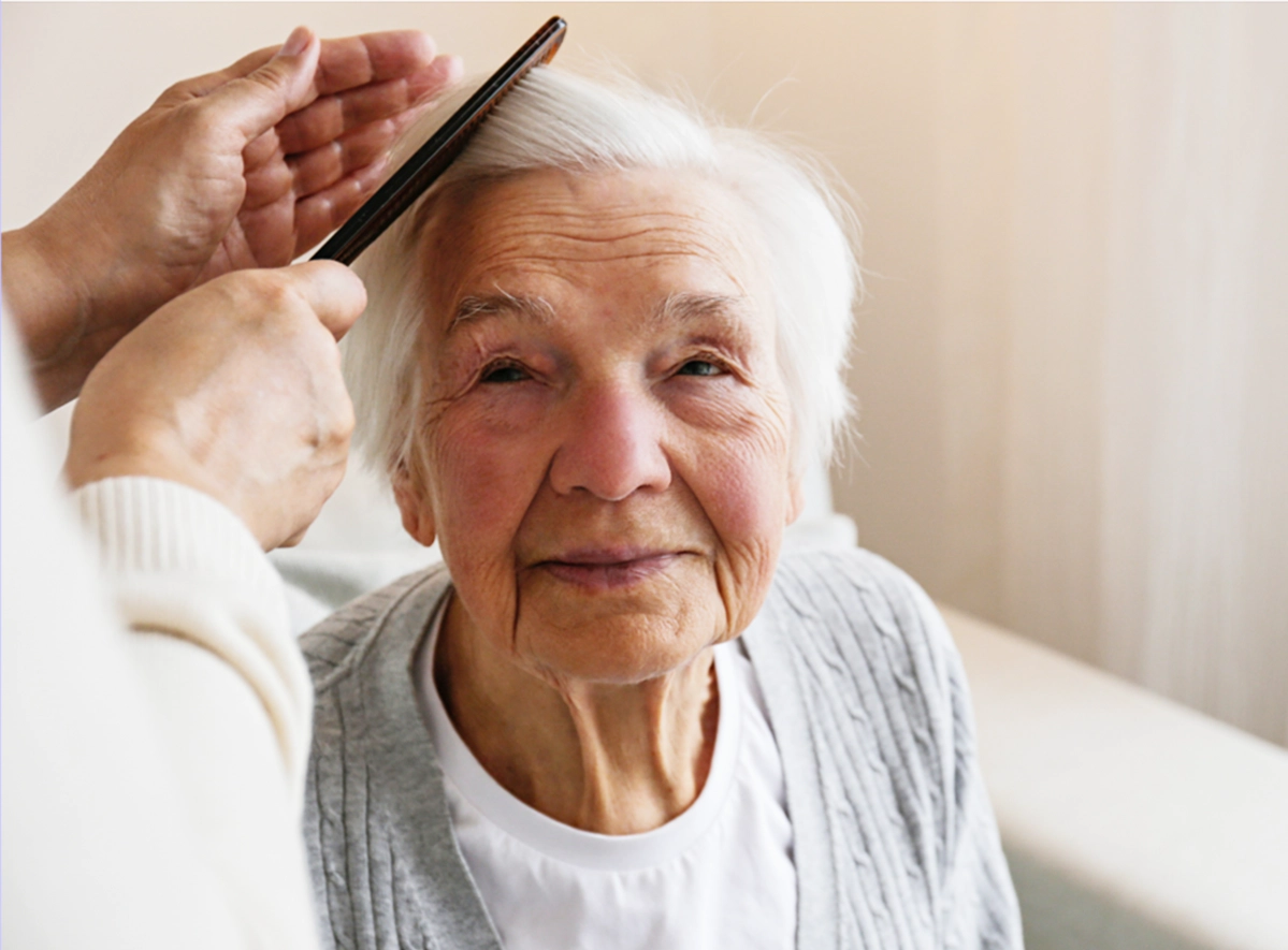 Smiling Elderly Woman with white hair getting her hair brushed by a care giver